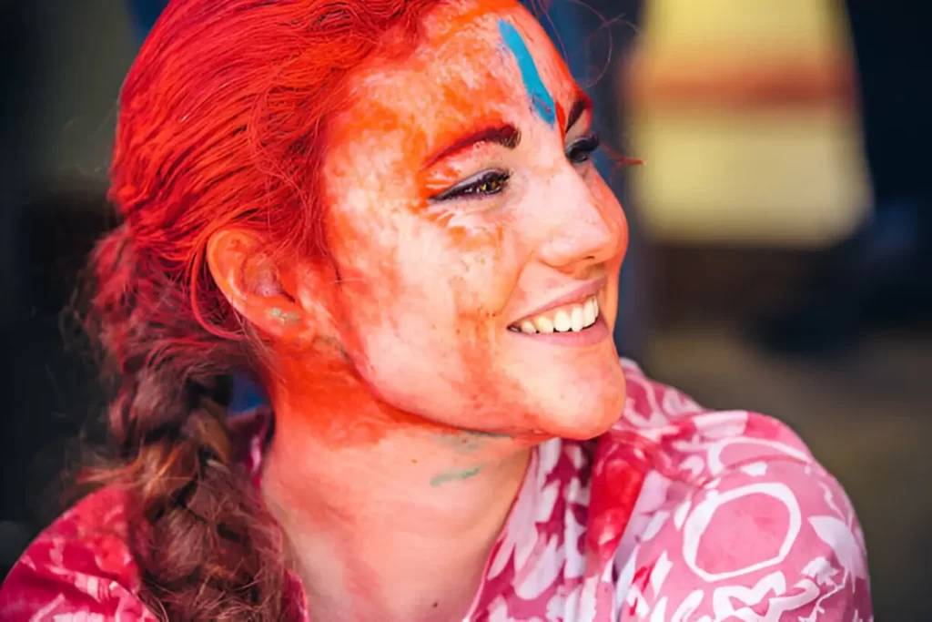 Woman, with her lowered sunglasses, is staring at the camera with her face all smeared with red color pigment during the Holi Festival in Jaipur, India.